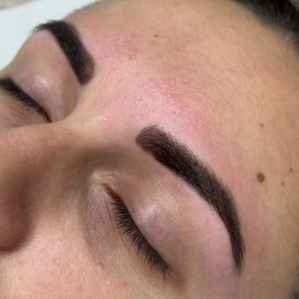 Close-up of both brows after a hybrid brow stain and wax, eyes closed: dark brown brows with a crisp waxed edge and the stain carried onto the skin for a filled-in look.