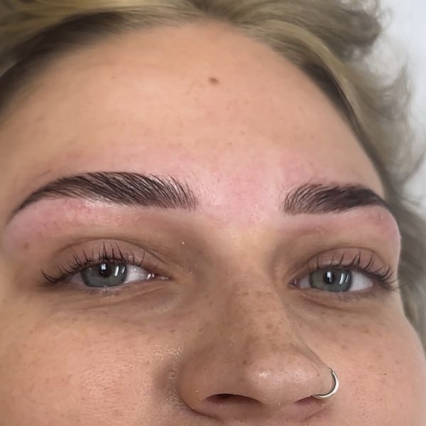 Both eyes of a blonde client after a brow lamination and Korean lash lift: brows brushed up and tinted, natural lashes curled up from the root.