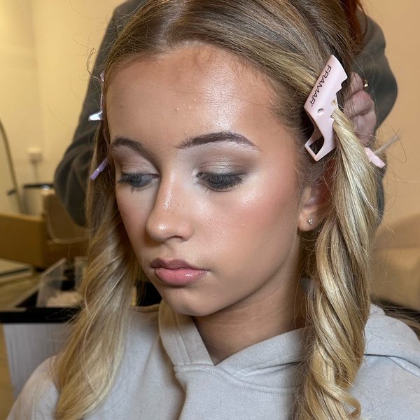 Soft glam make-up photographed in the salon with the hair held back in pink clips: warm shimmering bronze eyeshadow, a winged liner and a glossy pink lip.