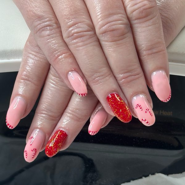 Christmas builder gel nails on both hands: medium almond nails in pale pink with red glitter accent nails and hand-painted candy cane stripes.