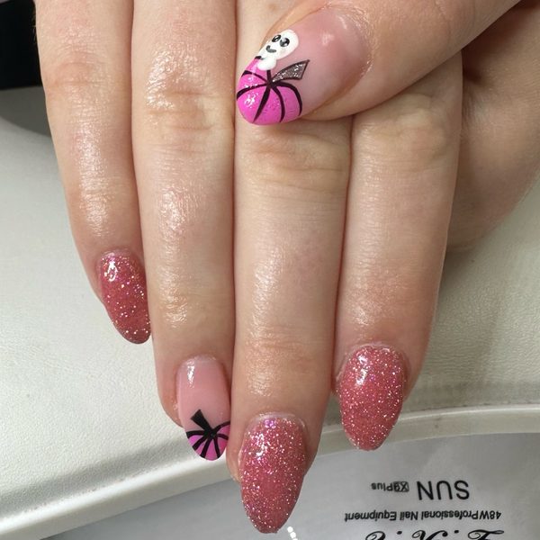 Dusky pink glitter builder gel nails with nude accent nails: one painted with a black bow, another with a pink and black spider web and a small ghost.