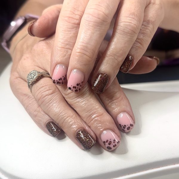 Builder gel nails in a nude pink base with hand-painted brown leopard print, set off by bronze glitter and dark brown accent nails.