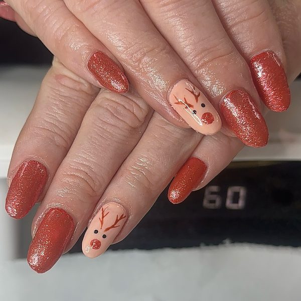 Christmas builder gel nails in rust-red glitter with a nude accent nail hand-painted as a reindeer face with antlers and a red nose.