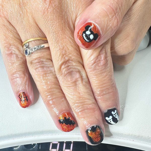 Halloween gel nails in orange and black glitter with hand-painted designs in orange, black and white across the accent nails.