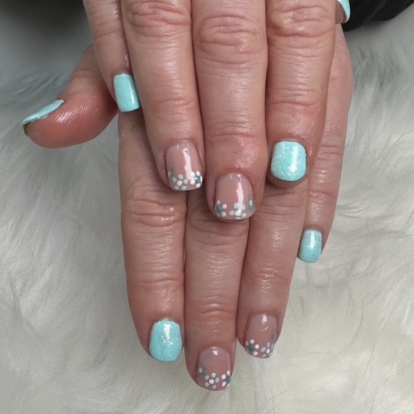 Short gel nails in mint green, some with glitter, alternating with nude nails finished in clusters of white and silver dots.